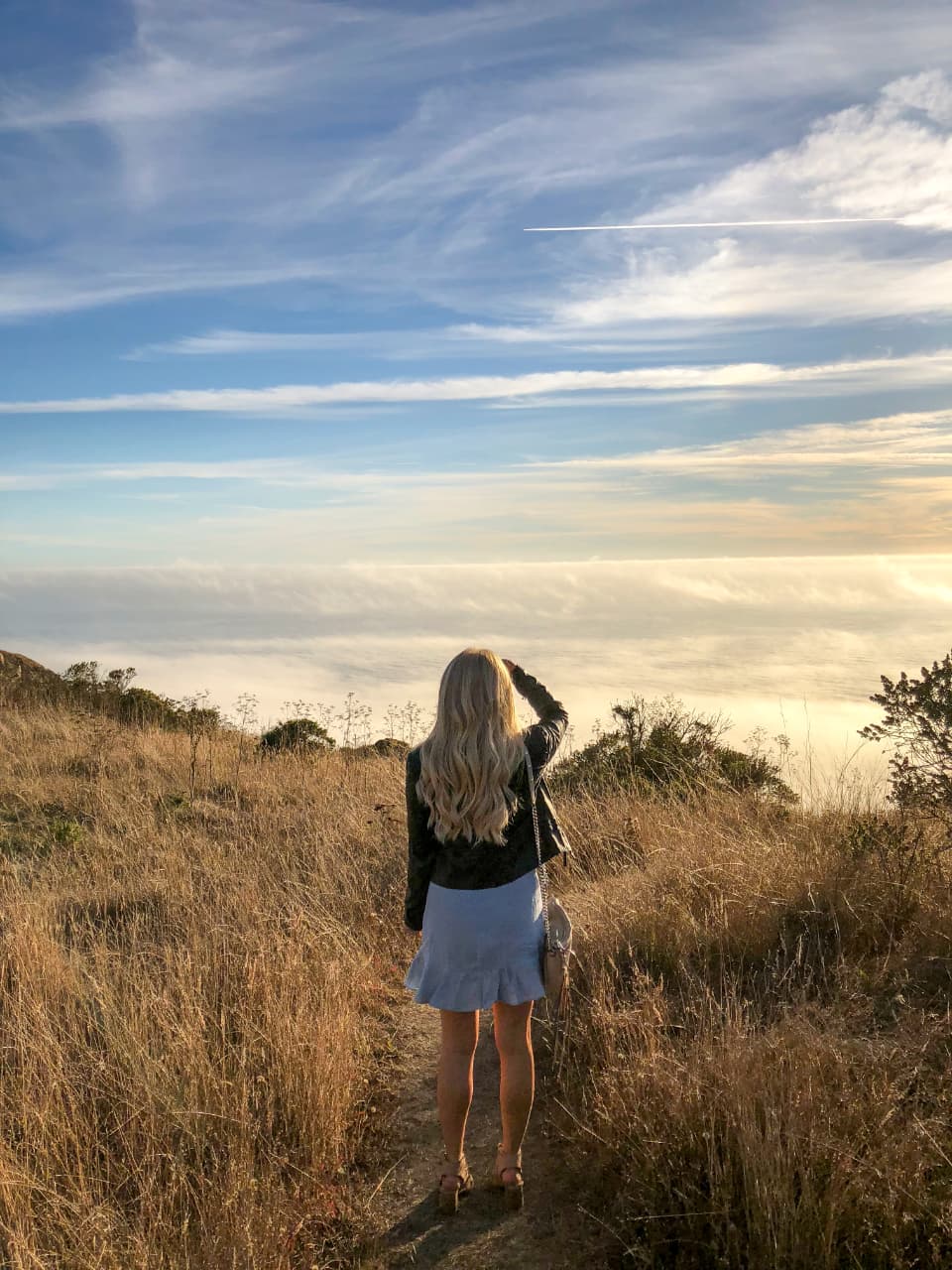 A person on a hilltop path looking out toward the horizon
