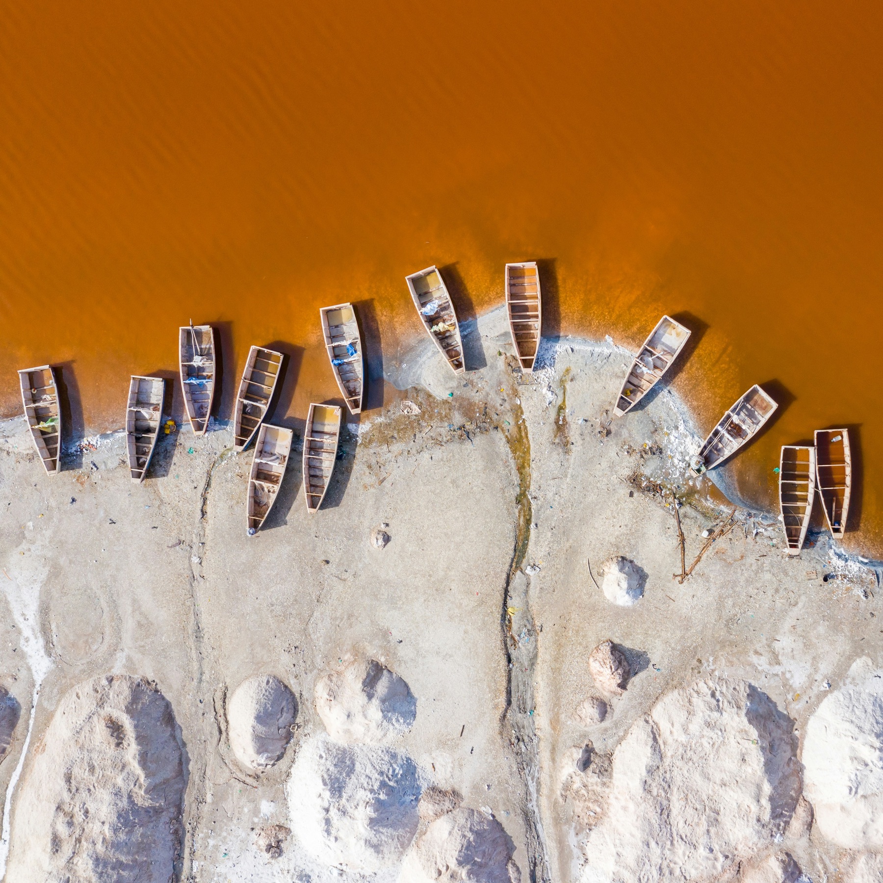 An aerial view of wooden fishing boats fanned along a vivid orange shoreline
