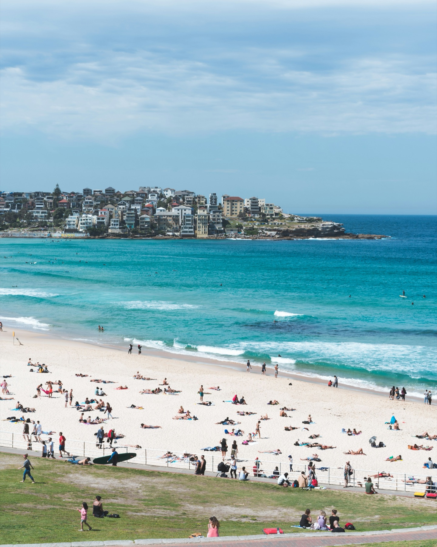 A turquoise bay and white-sand beach full of people on a bright afternoon