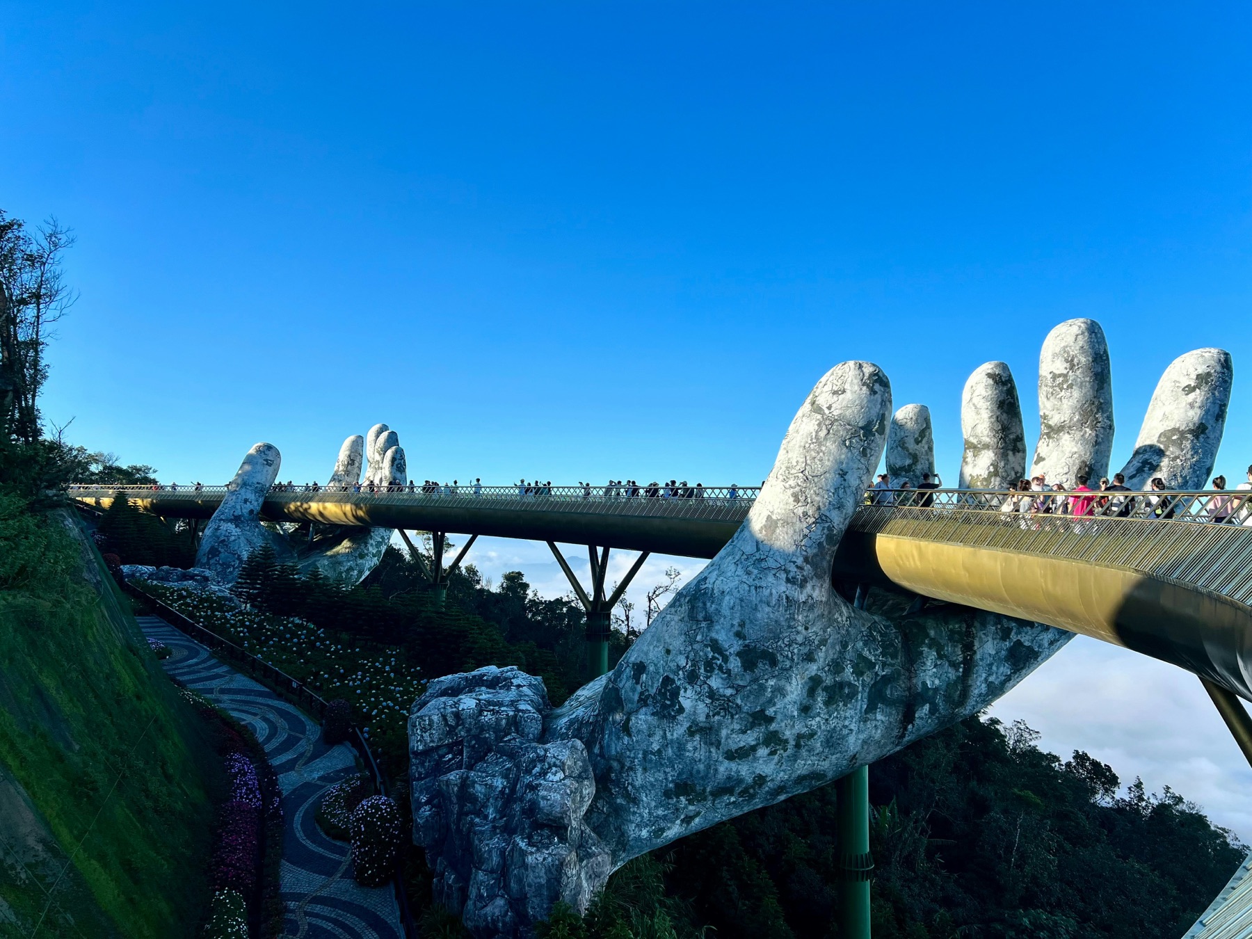 A golden walkway held aloft by giant stone hands, winding through mountain mist