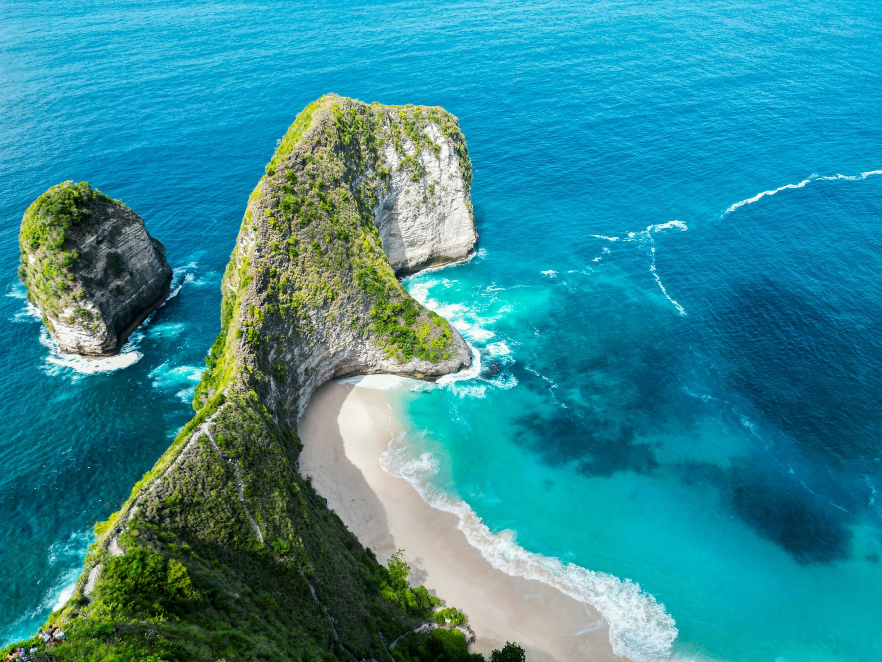A dramatic green cliff jutting into a deep blue ocean above a curved white-sand beach