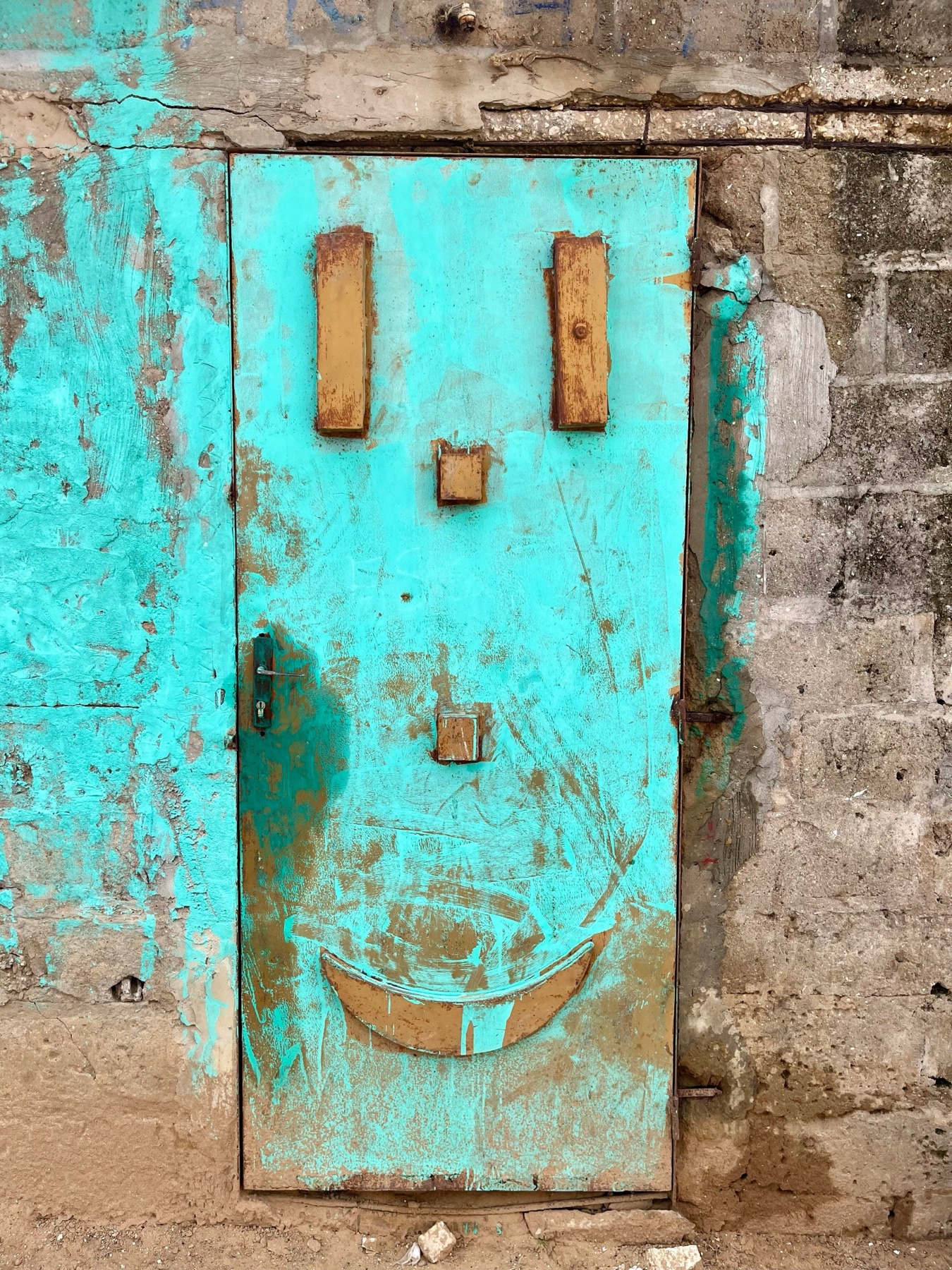 A weathered turquoise door whose rust marks form an accidental smile